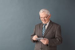 Senior man teacher wearing glasses studio standing isolated on gray using internet on digital tablet concentrated stock photo Senior man teacher wearing glasses studio standing isolated on gray using internet on digital tablet concentrated stock photo