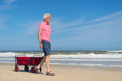 Senior man walking with red cart at beach stock photo Senior man walking with red cart at beach stock photo