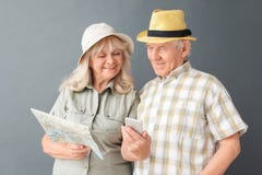 Senior tourists in beach hats studio standing on gray with map woman showing husband pictures on smartphone royalty free stock image Senior tourists in beach hats studio standing on gray with map woman showing husband pictures on smartphone royalty free stock image