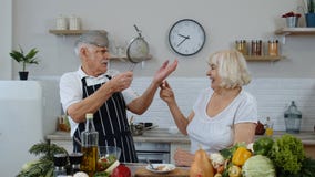 Senior woman and man making a funny dance with strainers. Dancing while cooking together in kitchen
