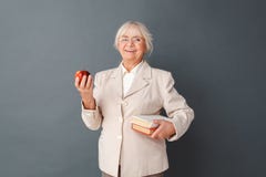 Senior woman in fromal suit and glasses studio standing on gray with books and apple laughing cheerful stock photography Senior woman in fromal suit and glasses studio standing on gray with books and apple laughing cheerful stock photography