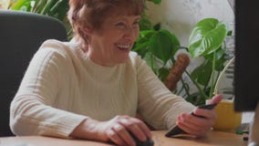 Senior woman working on computer, calling mobile, laughing