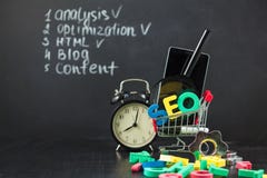 SEO Search engine optimization concept Colored letters of SEO with clock, magnifying , smartphone, gears in a basket on a black ba stock photo SEO Search engine optimization concept Colored letters of SEO with clock, magnifying , smartphone, gears in a basket on a black ba stock photo