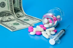 Seringue, dollars et pilules roses et blanches sur un fond bleu lumineux image stock Seringue, dollars et pilules roses et blanches sur un fond bleu lumineux image stock