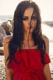 Sexig flicka med länge vått hår i den eleganta röda klänningen som poserar på stranden arkivbild Sexig flicka med länge vått hår i den eleganta röda klänningen som poserar på stranden arkivbild