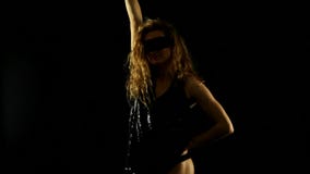 blonde woman with shining black top and masque dancing in the dark
