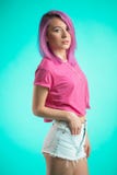 Señora tímida con el pelo rosado que presenta sobre música que escucha del fondo azul en auriculares Fotografía de archivo Señora tímida con el pelo rosado que presenta sobre música que escucha del fondo azul en auriculares Fotografía de archivo