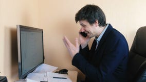 Sfrustowany mężczyzna pracuje przy komputerem i dzwoni telefon komórkowego Porównuje grafika na ekranie na papierze i zbiory wideo Sfrustowany mężczyzna pracuje przy komputerem i dzwoni telefon komórkowego Porównuje grafika na ekranie na papierze i zbiory wideo