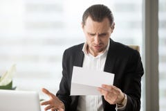 Sfrustowany młody biznesmen patrzeje bałamutnego list w offi obraz stock Sfrustowany młody biznesmen patrzeje bałamutnego list w offi obraz stock