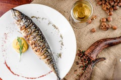 Sgombro arrostito con una fetta di limone su un piatto bianco ed e su un vetro di vino bianco su una tela di sacco Vista superior immagine stock libera da diritti Sgombro arrostito con una fetta di limone su un piatto bianco ed e su un vetro di vino bianco su una tela di sacco Vista superior immagine stock libera da diritti
