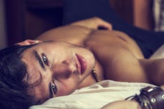 Shirtless sexig manlig modell som bara ligger på hans säng arkivbild Shirtless sexig manlig modell som bara ligger på hans säng arkivbild