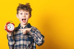 Shocked kid boy holding clock alarm, copy space. Kid isolated over yellow background. Time for school. Little student overslept. T. Ime concept. Excited boy at stock photos Shocked kid boy holding clock alarm, copy space. Kid isolated over yellow background. Time for school. Little student overslept. T. Ime concept. Excited boy at stock photos