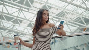 Shoppingkvinna som ler med påsar som talar på telefonen i galleria Härlig flicka med smartphonen i köpcentrum eller lager videofilmer Shoppingkvinna som ler med påsar som talar på telefonen i galleria Härlig flicka med smartphonen i köpcentrum eller lager videofilmer