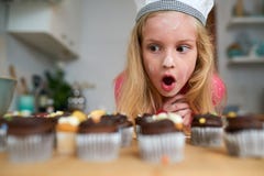 My first batch of cupcakes. Shot of a surprised little girl looking at cupcakes she baked at home.