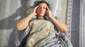 Sick man rubbing temples on bed stock images Sick man rubbing temples on bed stock images