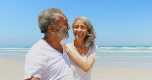 Side view of happy active senior African American couple walking on beach in the sunshine 4k