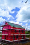 Side view of a new two-storey detached house under construction with red protective layer and scaffolding Stock Images Side view of a new two-storey detached house under construction with red protective layer and scaffolding Stock Images