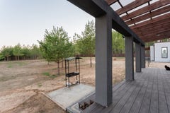 Side view of an open veranda in front of a modern forest cottage. Pine young forest under the sunset rays in the Stock Photo Side view of an open veranda in front of a modern forest cottage. Pine young forest under the sunset rays in the Stock Photo