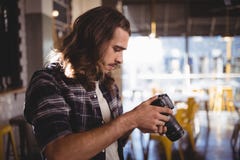 Side view of young male photographer holding DSLR camera. At coffee shop Royalty Free Stock Photography Side view of young male photographer holding DSLR camera. At coffee shop Royalty Free Stock Photography