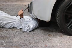 Sidosikt av mekanikern i den vita likformign som ner ligger och fixar under bilen Service för auto reparation arkivfoto Sidosikt av mekanikern i den vita likformign som ner ligger och fixar under bilen Service för auto reparation arkivfoto