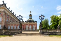 Sidosikten av Das Neue Palast, parkerar in Sanssouci, Potsdam, Tyskland med dess trappa som ingången, de falska järnlyktorna och royaltyfri bild Sidosikten av Das Neue Palast, parkerar in Sanssouci, Potsdam, Tyskland med dess trappa som ingången, de falska järnlyktorna och royaltyfri bild