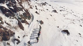Siete viajeros est?n en una formaci?n al pico de una colina nevada, de una manera ayuda a su engranaje y mochilas con metrajes Siete viajeros est?n en una formaci?n al pico de una colina nevada, de una manera ayuda a su engranaje y mochilas con metrajes