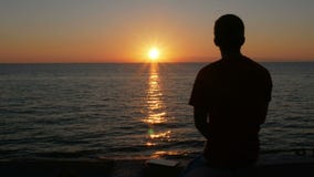 Silhouet van een mens bij zonsondergang op het strand van de oceaan Een mens bewondert de oranje zon is bijna plaatste stock footage Silhouet van een mens bij zonsondergang op het strand van de oceaan Een mens bewondert de oranje zon is bijna plaatste stock footage