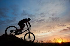 Silhouette of bicyclist wearing helmet and sportswear on mountain bike coming down the hill at sunset stock photography Silhouette of bicyclist wearing helmet and sportswear on mountain bike coming down the hill at sunset stock photography