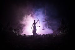 Silhouette de statue géante brouillée de justice de dame avec l'épée et d'échelle se tenant derrière la foule la nuit avec le fon images libres de droits Silhouette de statue géante brouillée de justice de dame avec l'épée et d'échelle se tenant derrière la foule la nuit avec le fon images libres de droits