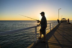 Silhouette of fisherman with hat and fish rod standing on sea dock fishing at sunset with beautiful orange sky in vacations relax royalty free stock photo Silhouette of fisherman with hat and fish rod standing on sea dock fishing at sunset with beautiful orange sky in vacations relax royalty free stock photo
