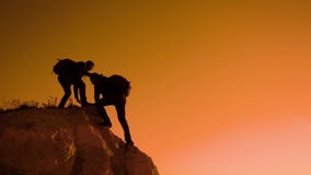 Silhouette two men teamwork tourists climber climbs a mountain. walking tourist hiking adventure climbers sunset climb