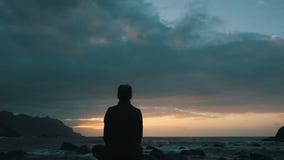 Silhouette of a woman sitting on rocks at sunset observing ocean waves at Benijo beach in Tenerife, Canary Islands. stock footage Silhouette of a woman sitting on rocks at sunset observing ocean waves at Benijo beach in Tenerife, Canary Islands. stock footage
