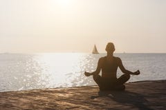 Silhouette of a young athletic girl who is engaged in yoga at sunrise on the beach with a sailboat royalty free stock photo Silhouette of a young athletic girl who is engaged in yoga at sunrise on the beach with a sailboat royalty free stock photo