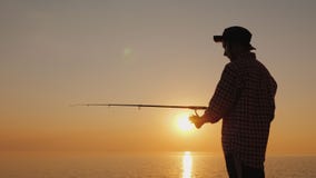 Silhouette of a young fisherman fishing on the beach at sunset. Side view stock photo Silhouette of a young fisherman fishing on the beach at sunset. Side view stock photo