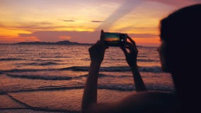 Silhouette of young tourist woman photographs ocean view with smartphone during sunset at beach stock photos Silhouette of young tourist woman photographs ocean view with smartphone during sunset at beach stock photos