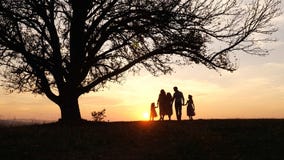 Silhouettes of happy family walking in the meadow near a big tree during sunset. Royalty Free Stock Images Silhouettes of happy family walking in the meadow near a big tree during sunset. Royalty Free Stock Images
