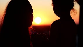 Silhouettes of mother and her daughter heads. Mom and child looking at the sun