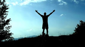 Silhouettieren Sie Läufe des jungen Mannes bis zur Spitze des Berges und der Erhebunger seine Hände als Zeichen der Leistung, des Silhouettieren Sie Läufe des jungen Mannes bis zur Spitze des Berges und der Erhebunger seine Hände als Zeichen der Leistung, des