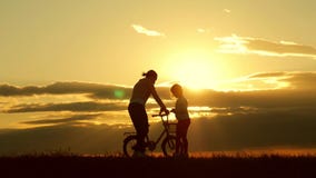 Silhouettieren Sie reizende Familie des Radfahrers auf der Wiese zur Sonnenuntergangzeit Schattenbild der Mutter und des Babys, d stock video footage Silhouettieren Sie reizende Familie des Radfahrers auf der Wiese zur Sonnenuntergangzeit Schattenbild der Mutter und des Babys, d stock video footage