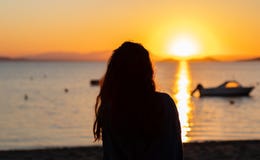 Silhueta de uma jovem mulher na frente de um por do sol na praia, com barcos e montanhas As f?rias relaxam a cena em mar?o Menor, imagens de stock Silhueta de uma jovem mulher na frente de um por do sol na praia, com barcos e montanhas As f?rias relaxam a cena em mar?o Menor, imagens de stock