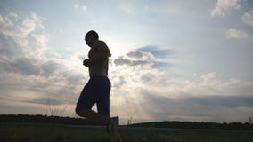 Silhueta do homem muscular que movimenta-se na estrada secundária no por do sol Treinamento masculino do basculador para exterior video estoque Silhueta do homem muscular que movimenta-se na estrada secundária no por do sol Treinamento masculino do basculador para exterior video estoque