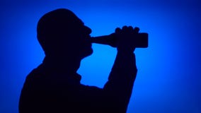 Silueta de la botella de cerveza de la abertura del hombre mayor en fondo azul Cara masculina del ` s en la consumición del perfi almacen de video Silueta de la botella de cerveza de la abertura del hombre mayor en fondo azul Cara masculina del ` s en la consumición del perfi almacen de video