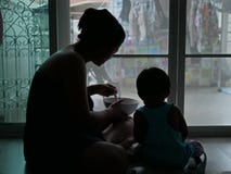 Silueta de la madre asiática que sostiene un cuenco de comida y que alimenta a su bebé en casa fotografía de archivo Silueta de la madre asiática que sostiene un cuenco de comida y que alimenta a su bebé en casa fotografía de archivo