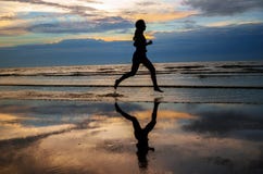 Silueta del basculador de la mujer que corre en la playa de la puesta del sol con la reflexión foto de archivo libre de regalías Silueta del basculador de la mujer que corre en la playa de la puesta del sol con la reflexión foto de archivo libre de regalías