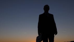 Silueta del hombre de negocios con la cartera que camina en la puesta del sol, contra un cielo azul almacen de video Silueta del hombre de negocios con la cartera que camina en la puesta del sol, contra un cielo azul almacen de video