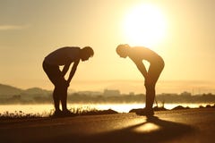Siluette esaurite e stanche delle coppie di forma fisica al tramonto fotografia stock Siluette esaurite e stanche delle coppie di forma fisica al tramonto fotografia stock