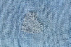 Silver heart on a blue background of cotton fabric. Romantic pastel background. Design with copy space. Denim color stock photography Silver heart on a blue background of cotton fabric. Romantic pastel background. Design with copy space. Denim color stock photography