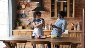Joyful millennial black couple have fun at kitchen singing aloud