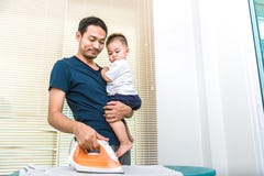 Single dad is ironing while carrying his son. People and Lifestyles concept. stock photography Single dad is ironing while carrying his son. People and Lifestyles concept. stock photography