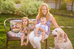Sira de mãe e suas crianças que relaxam no jardim com cão de estimação Família feliz que joga com seu cão de labrador retriever n fotografia de stock royalty free Sira de mãe e suas crianças que relaxam no jardim com cão de estimação Família feliz que joga com seu cão de labrador retriever n fotografia de stock royalty free
